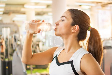Photo for Young athletic woman drinking water in a gym - Royalty Free Image