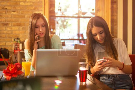 Téléchargez les photos : Adolescentes utilisant des téléphones tout en passant du temps ensemble dans un café - en image libre de droit