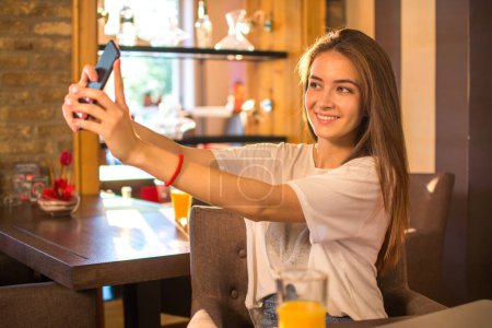 Foto de Sonriente adolescente utilizando el teléfono móvil para hacer foto selfie para las redes sociales - Imagen libre de derechos