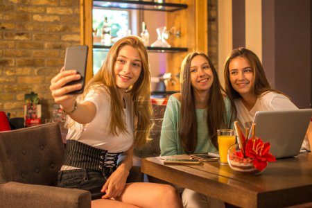 Foto de Adolescentes tomando divertidos selfies juntos en un café - Imagen libre de derechos