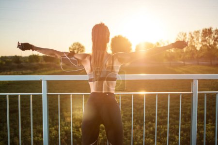 Téléchargez les photos : Fitness femme levant les bras pour célébrer le succès de l'entraînement et la liberté contre le coucher du soleil ciel à l'extérieur
. - en image libre de droit