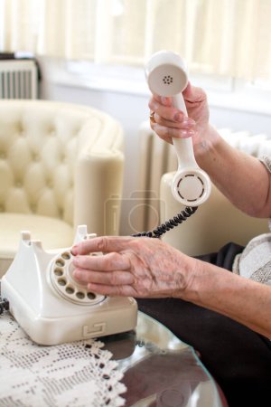Photo for Close-up of wrinkled senior womans hands dialing a phone number on retro cable telephone. - Royalty Free Image