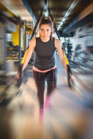 Photo for Sporty woman doing arm exercises with suspension straps at gym. Blurred motion effect - Royalty Free Image