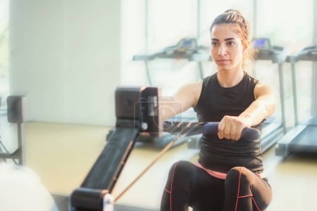 Téléchargez les photos : Femme faisant de l'exercice sur rameur dans la salle de gym - en image libre de droit