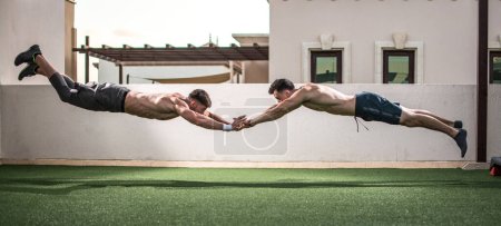 Téléchargez les photos : Deux beaux hommes musclés faisant des pompes avec des sauts à l'extérieur. Hommes sportifs tenant la main tout en sautant ensemble. - en image libre de droit