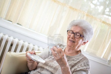 Foto de Feliz anciana disfrutando de una taza de café mientras está sentada en el sofá en casa. - Imagen libre de derechos