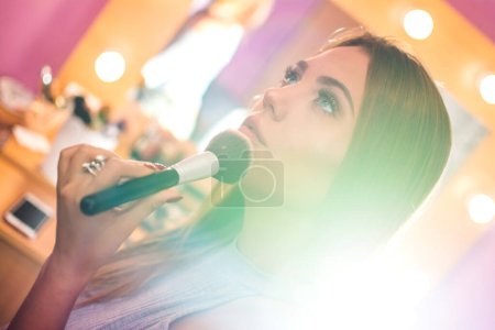 Téléchargez les photos : Jeune femme qui applique le maquillage au pinceau. Effet d'éclairage sur la photo. - en image libre de droit