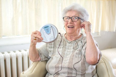 Cheerful senior woman listening to music on CD player at home.