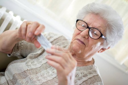 Close-up portrait of senior woman with glasses reading pills expiration date.