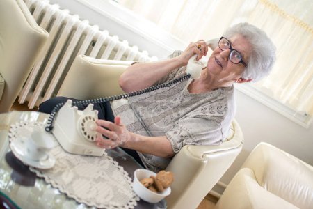 Téléchargez les photos : Heureuse femme âgée parlant sur un téléphone rétro à la maison. - en image libre de droit