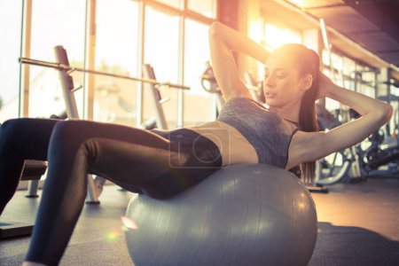 Téléchargez les photos : Jeune femme en forme faisant des sit-ups sur le ballon d'exercice dans la salle de gym
. - en image libre de droit