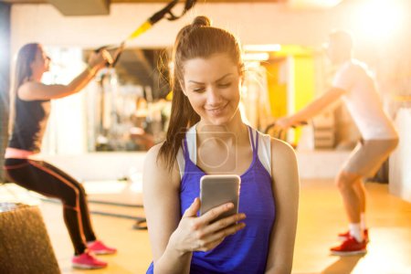 Téléchargez les photos : Fille textos tout en prenant une pause dans une salle de gym - en image libre de droit