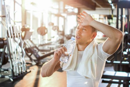 Téléchargez les photos : Homme sportif fatigué boire de l'eau à la salle de gym. - en image libre de droit