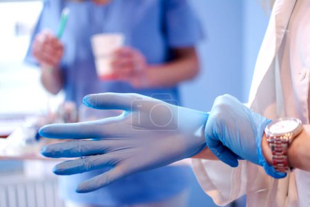 Foto de Primer plano de las manos de las médicas que se ponen guantes quirúrgicos esterilizados azules en la clínica médica - Imagen libre de derechos