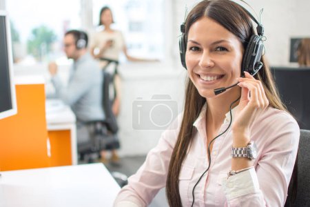 Téléchargez les photos : Opérateur de ligne téléphonique amicale avec écouteurs dans le centre d'appel. - en image libre de droit