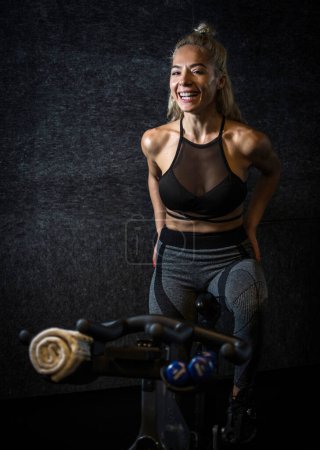 Foto de Deportista alegre en bicicleta estática sobre fondo oscuro. - Imagen libre de derechos