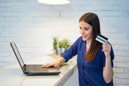 glückliche junge Frau kauft online mit Kreditkarte und Laptop ein