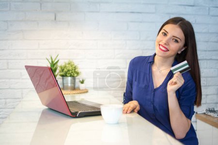Téléchargez les photos : Joyeux jeune femme shopping en ligne avec carte de crédit et ordinateur portable à la maison - en image libre de droit