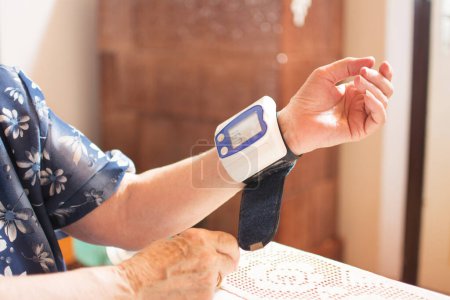 Großaufnahme einer Seniorin, die am Tisch Blutdruck misst