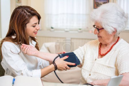Foto de Enfermera haciendo monitoreo de presión arterial para mujeres mayores en casa - Imagen libre de derechos