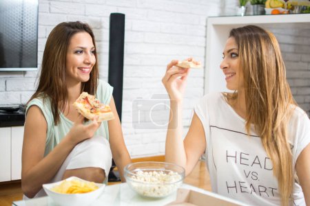 Téléchargez les photos : Concept de restauration rapide. Les jeunes femmes mangent des pizzas, des collations et des chips à la maison - en image libre de droit