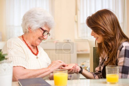 Téléchargez les photos : Femme âgée essayant de lire la chiromancie de sa petite-fille tout en ayant du jus d'orange ensemble à la maison - en image libre de droit