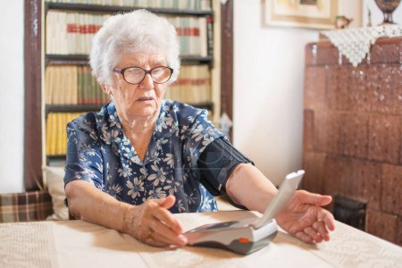 Téléchargez les photos : Femme âgée mesurant sa tension artérielle à la maison - en image libre de droit