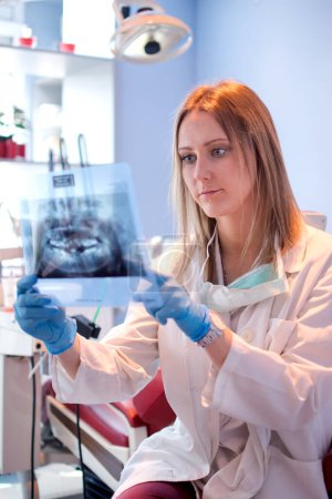 Foto de Dentista femenina examinando imagen de rayos X de dientes en clínica dental - Imagen libre de derechos