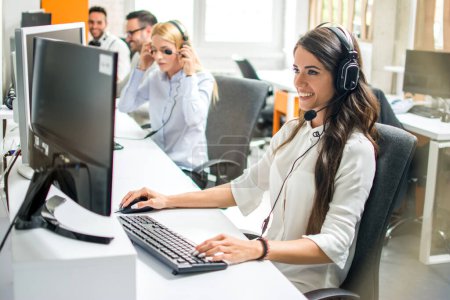 Photo for Young employee working with a headset accompanied by her team in call center - Royalty Free Image