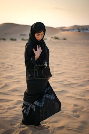 Téléchargez les photos : Arabe musulmane en robe noire traditionnelle marchant dans le désert. - en image libre de droit