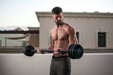 Photo for Shirtless muscular man doing exercises with barbell outdoors. - Royalty Free Image