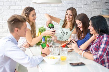 Téléchargez les photos : Groupe de cinq amis qui s'amusent en cuisine. Ils boivent du vin rouge et préparent un repas - en image libre de droit
