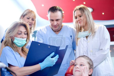 Téléchargez les photos : Groupe de dentistes analysant le rapport médical de la jeune fille patiente au cabinet dentaire - en image libre de droit