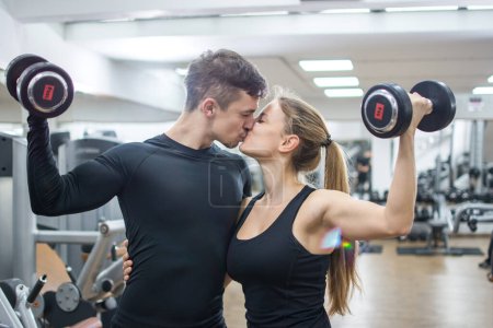Photo for Beautiful young couple with weights kissing in the gym. - Royalty Free Image