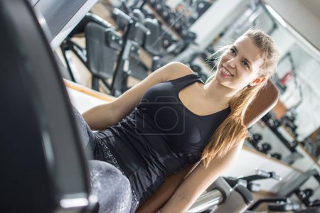 Téléchargez les photos : Souriant fille sportive travaillant sur la machine d'exercice dans la salle de gym. - en image libre de droit