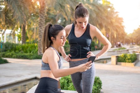 Foto de Sofá femenino mostrando a su cliente nuevos ejercicios por teléfono al aire libre - Imagen libre de derechos