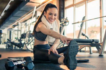 Photo for Smiling fitness girl touching toes and stretching her hands and legs at gym. - Royalty Free Image