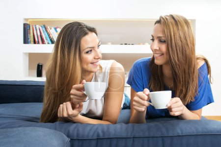 Téléchargez les photos : Sœurs jumelles avec tasses à café profitant d'une conversation dans le salon à la maison - en image libre de droit