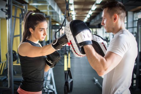 Téléchargez les photos : Jeune femme sportive frappant son partenaire masculin avec des gants de boxe rouges au gymnase - en image libre de droit