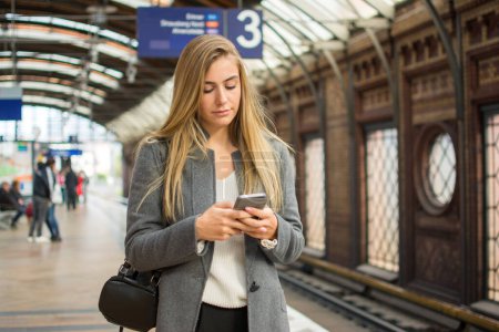 Photo for Young woman using phone at train station. - Royalty Free Image