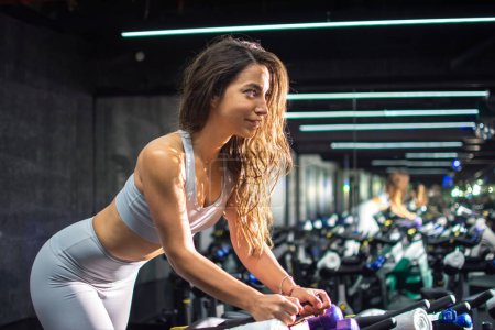 Photo for Side view portrait on beautiful young woman riding on the spinning bike at gym. - Royalty Free Image