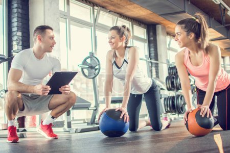 Photo for Gym instructor assisting two sporty women with pilates balls in fitness center. - Royalty Free Image