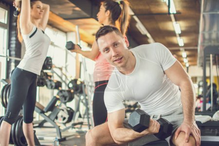 Téléchargez les photos : Beau jeune homme soulevant des poids dans une salle de gym. - en image libre de droit