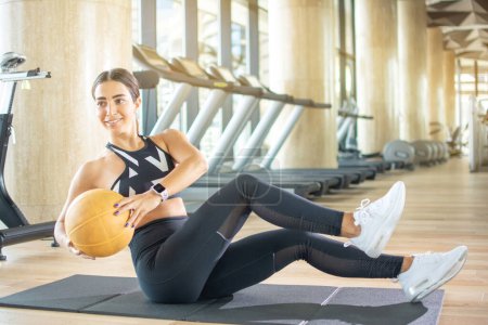 Téléchargez les photos : Fitness femme faire des exercices avec balle sur tapis d'exercice dans la salle de gym - en image libre de droit