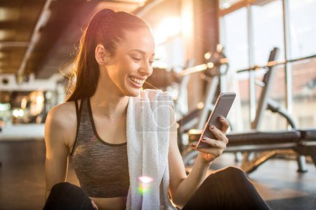 Photo for Young fit woman using smartphone at gym. - Royalty Free Image