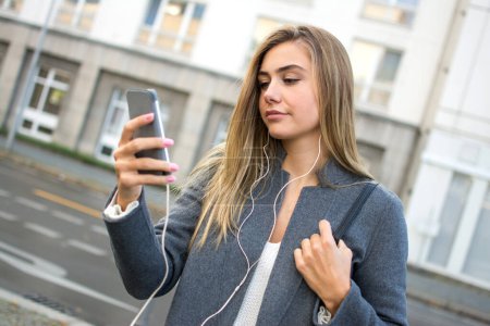 Foto de Hermosa joven mujer caminando por la calle y escuchando música desde el teléfono inteligente. - Imagen libre de derechos
