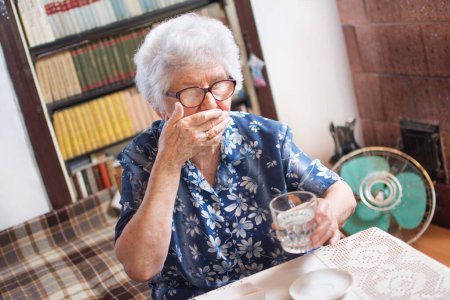 Téléchargez les photos : Femme âgée prenant des médicaments avec un verre d'eau - en image libre de droit