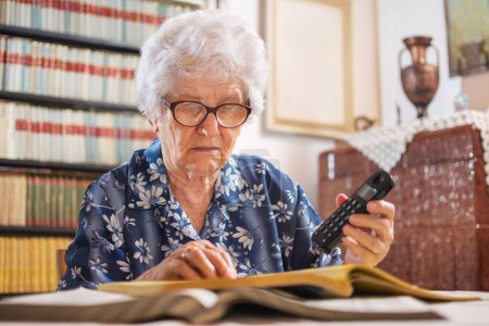 Senior woman searching book for services and holding telephone