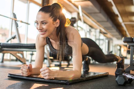Foto de Atractiva chica de fitness haciendo ejercicio tablón en la estera en el gimnasio. - Imagen libre de derechos