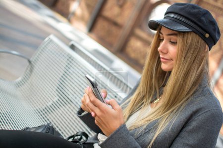 Téléchargez les photos : Portrait de fille avec chapeau en utilisant un téléphone portable à la gare. - en image libre de droit